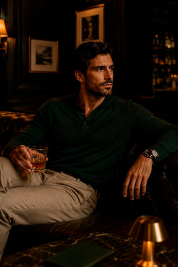 Man in a dark green polo and stone chinos relaxing on a leather sofa